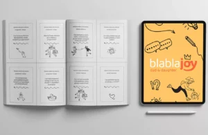 Na zdjęciu znajduje się otwarta książka z kartami do komunikacji dla taty z córką. Obok leży tablet z rysikiem, na którym wyświetlany jest napis „Blablajoy Dad & Daughter”.